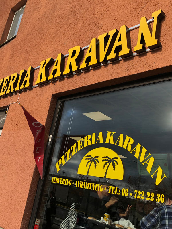 Bild fotad underifrån som visar Pizzeria Karavans gula skylt och exteriör